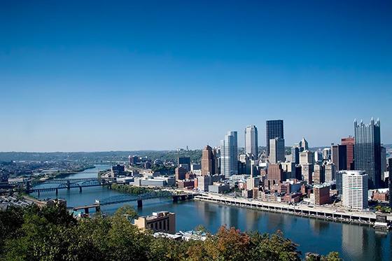 Photo of the Pittsburgh, Pennsylvania skyline featuring tall buildings, rivers, bridges, and blue skies