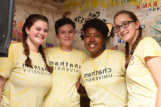 Photo of four students in matching yellow Chatham University shirts, posing together in Rea Coffeehouse