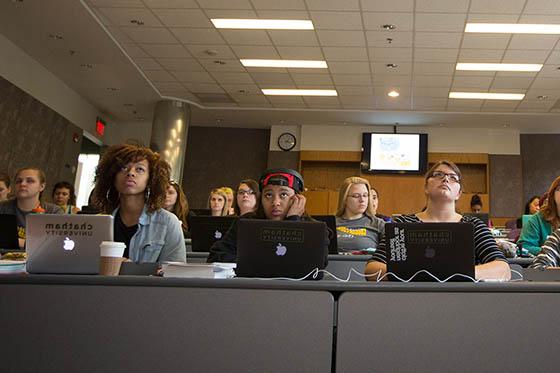 Photo of Chatham University students sitting in a lecture hall taking notes on laptops in tiered seating.