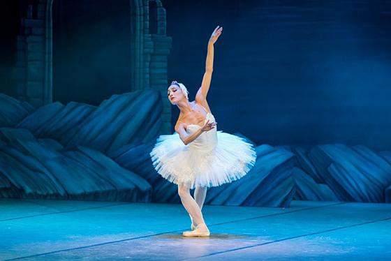 Photo of a ballerina dancing in Swan Lake, wearing a white costume and head piece. 