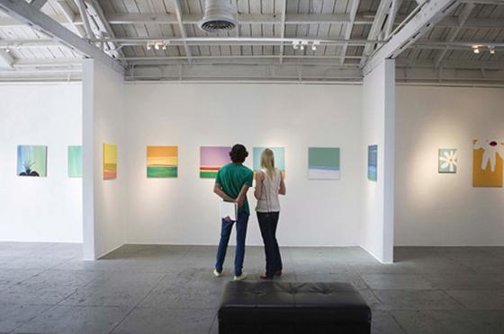 Photo of two young people standing in an art exhibit looking at colorful 绘画s on the white walls. 