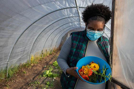 Photo of a female Chatham University student holding a bowl of harvested produce at the door of a greenhouse on Eden Hall Campus