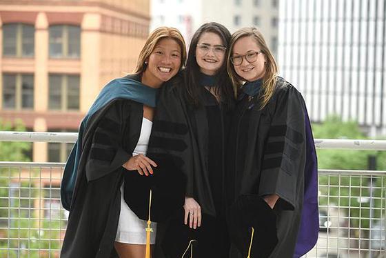 Photo of a graduating Chatham University student wearing a rainbow stole, with an arm over the shoulder of a parent or guardian