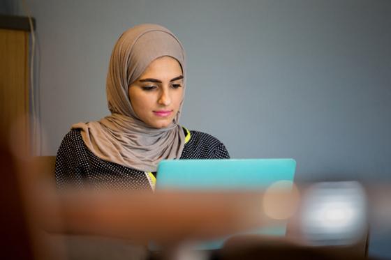 Photo of a female Chatham University wearing a hijab working on her computer in Cafe Rachel