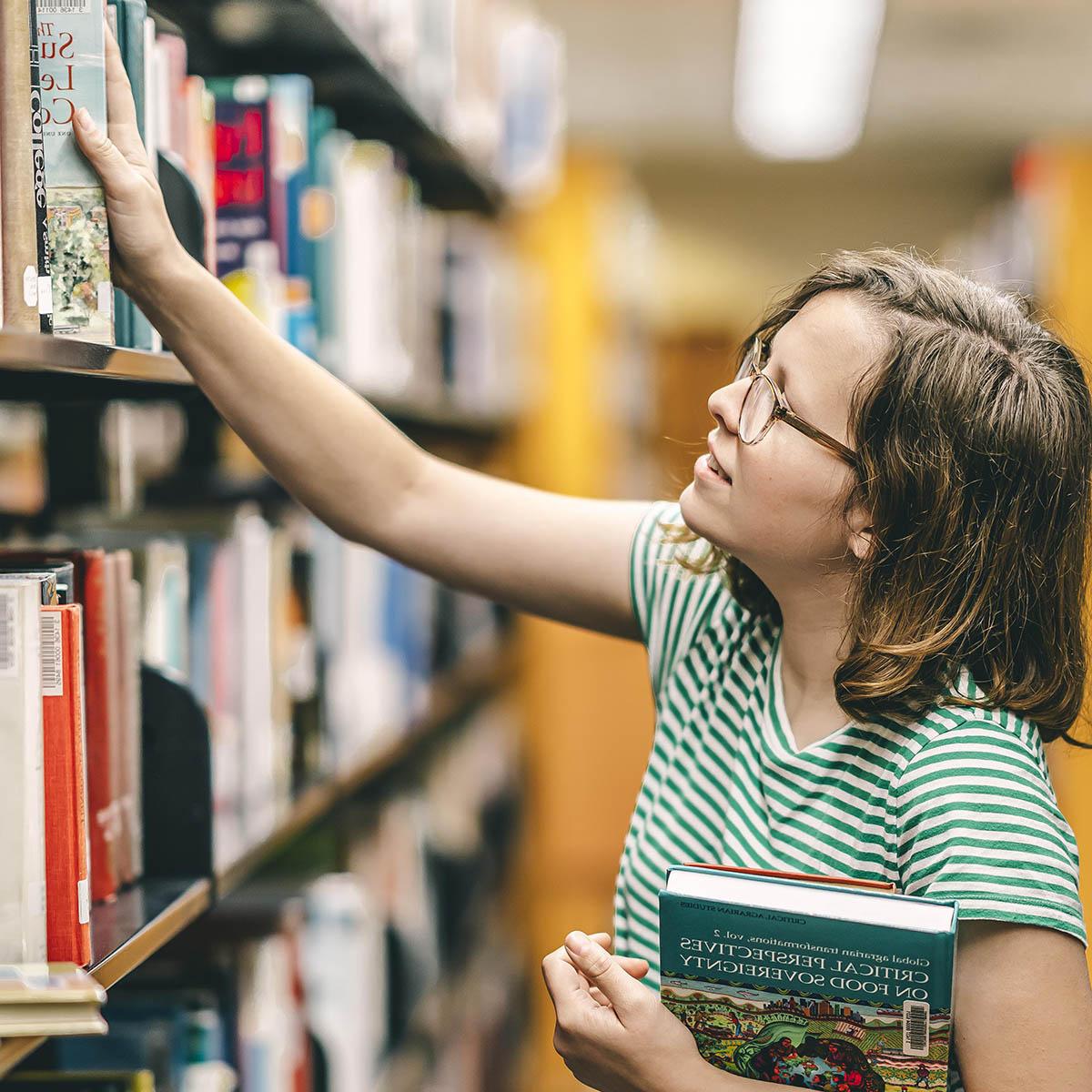 Photo of a student pulling a book off of a library shelf