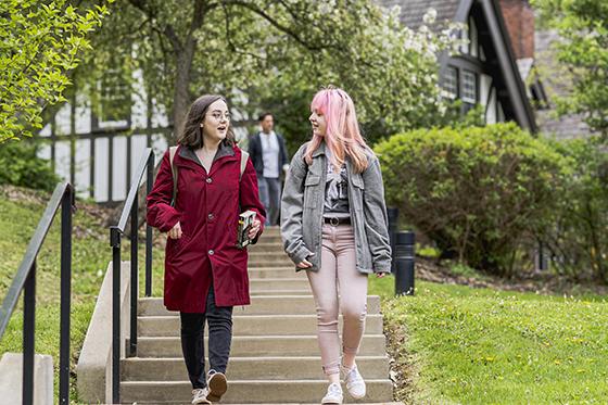 Photo of two Chatham University students walking across the Shadyside Campus, talking and walking down stairs
