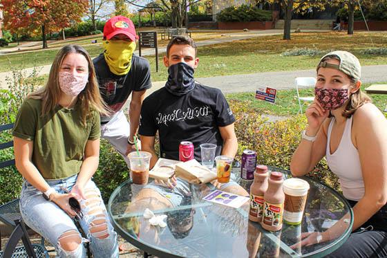 Photo of four Chatham University students in masks, hanging out together outside on Shadyside Campus
