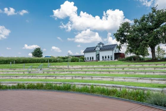 Chatham University's Eden Hall campus amphitheater with rows of built-in shelves sits at the bottom of a hill looking up to a white dairy barn with a solar panel roof. 