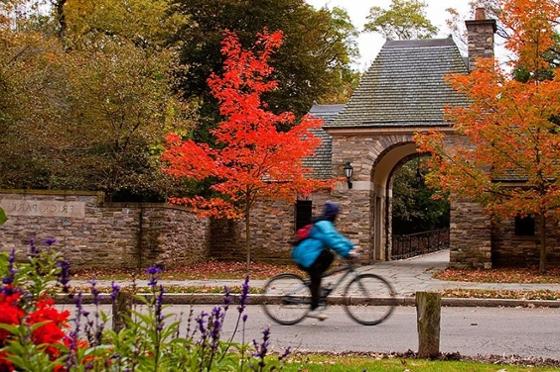 Photo of a bicyclist passing stone entrance to Frick Park in Pittsburgh framed by colorful fall foliage. 